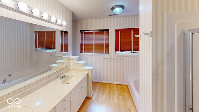 bathroom featuring wallpapered walls, double vanity, wood finished floors, a bath, and a sink