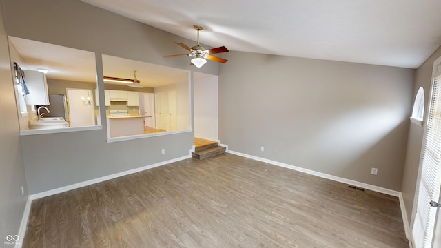 unfurnished living room featuring visible vents, lofted ceiling, a ceiling fan, wood finished floors, and baseboards