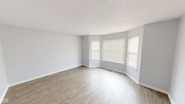 spare room with visible vents, wood finished floors, baseboards, and a textured ceiling