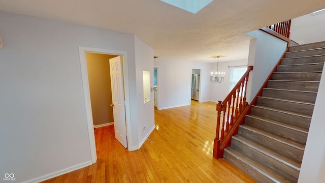 stairway featuring hardwood / wood-style floors, an inviting chandelier, a skylight, and baseboards