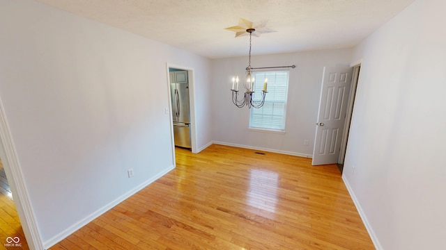 spare room with a chandelier, visible vents, light wood finished floors, and baseboards