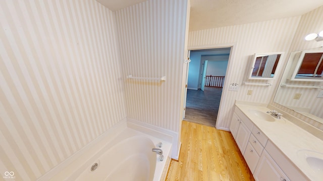 full bathroom featuring wallpapered walls, double vanity, wood finished floors, a bath, and a sink