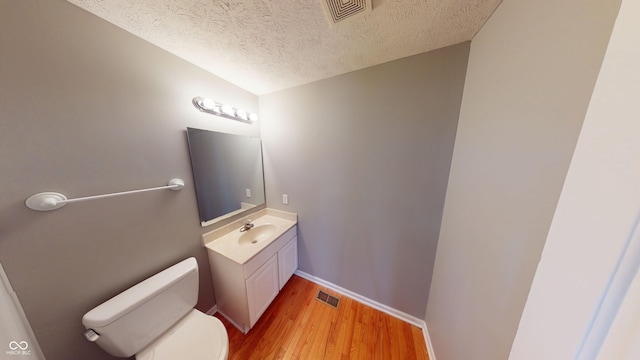 half bathroom with visible vents, toilet, wood finished floors, and vanity