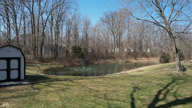 view of yard with a forest view, a water view, an outbuilding, and a storage shed