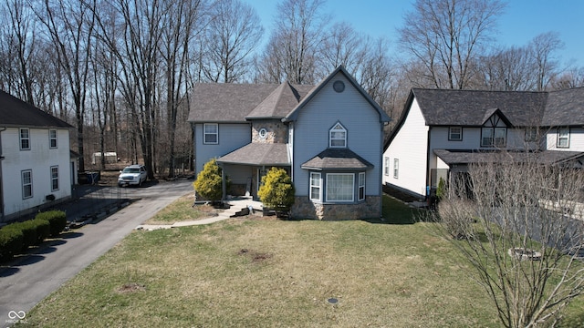 traditional-style house with stone siding, a front yard, and a shingled roof