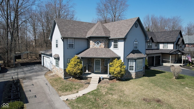 view of front of home with a front yard, roof with shingles, covered porch, concrete driveway, and stone siding