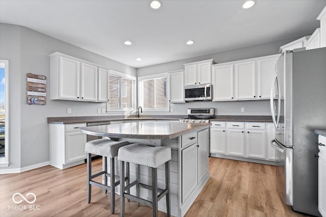 kitchen with a sink, appliances with stainless steel finishes, white cabinetry, light wood-type flooring, and a kitchen bar