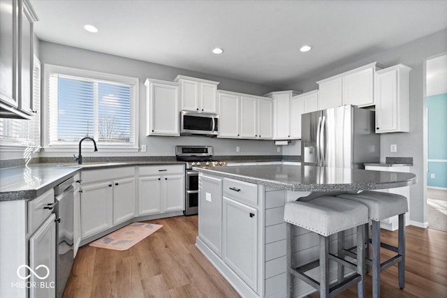 kitchen featuring a sink, wood finished floors, a center island, white cabinetry, and stainless steel appliances