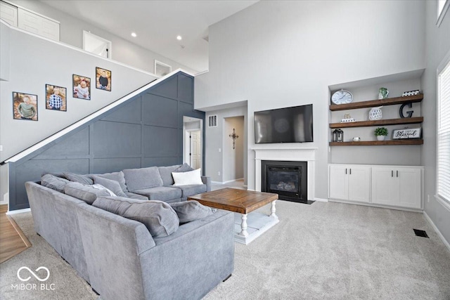 living room with built in shelves, visible vents, a fireplace with flush hearth, a towering ceiling, and light carpet