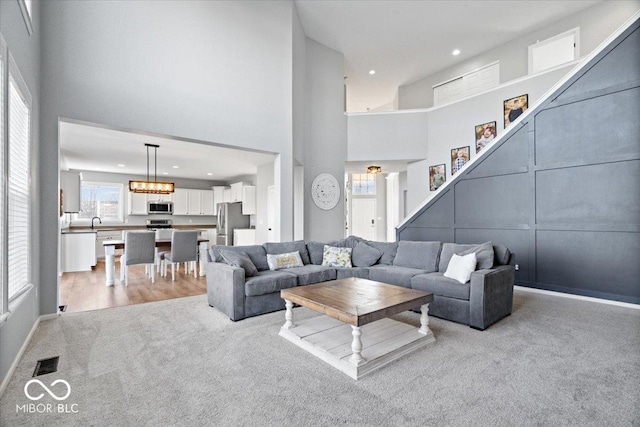 living room featuring recessed lighting, visible vents, light colored carpet, and a towering ceiling