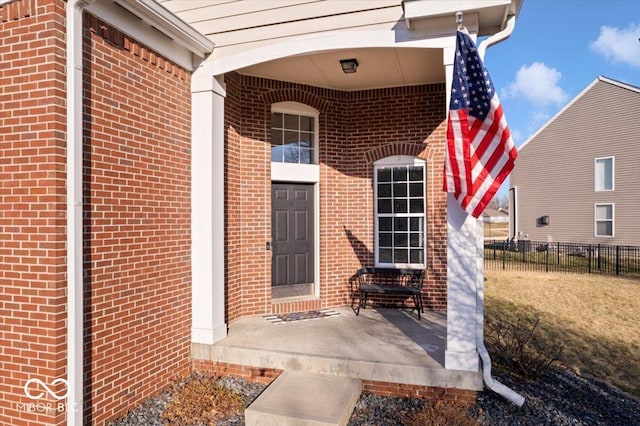 view of exterior entry with brick siding and fence