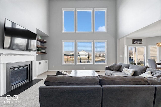 carpeted living room featuring a high ceiling, a fireplace with flush hearth, and baseboards