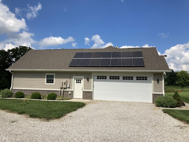 view of front of house with gravel driveway, a garage, brick siding, and roof mounted solar panels