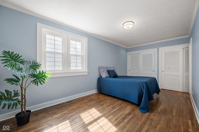 bedroom featuring visible vents, two closets, hardwood / wood-style floors, crown molding, and baseboards