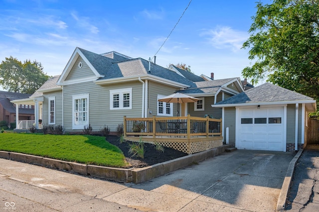 view of front of house featuring a shingled roof, a front yard, a deck, an outbuilding, and driveway