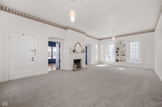 unfurnished living room featuring built in shelves, baseboards, a fireplace with flush hearth, carpet floors, and arched walkways