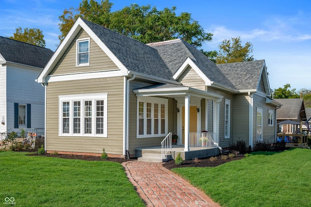 view of front of house with covered porch, a shingled roof, a front lawn, and fence