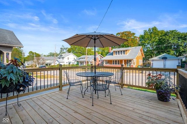 wooden deck featuring outdoor dining space, an outbuilding, a garage, and a residential view