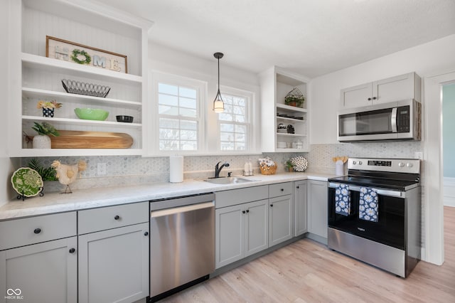 kitchen featuring gray cabinetry, open shelves, light wood-style flooring, appliances with stainless steel finishes, and a sink