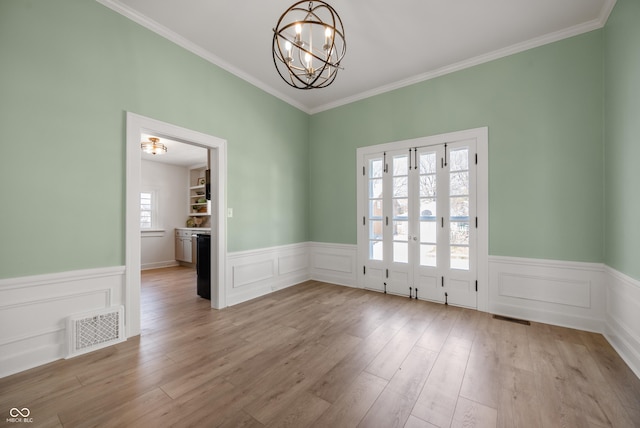 unfurnished dining area with a wainscoted wall, light wood-style flooring, visible vents, and a chandelier