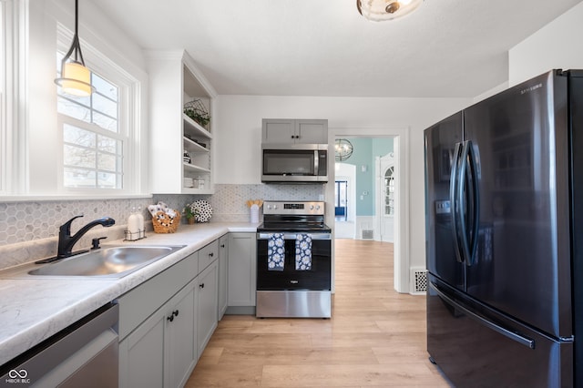 kitchen with a sink, light countertops, appliances with stainless steel finishes, light wood-style floors, and open shelves