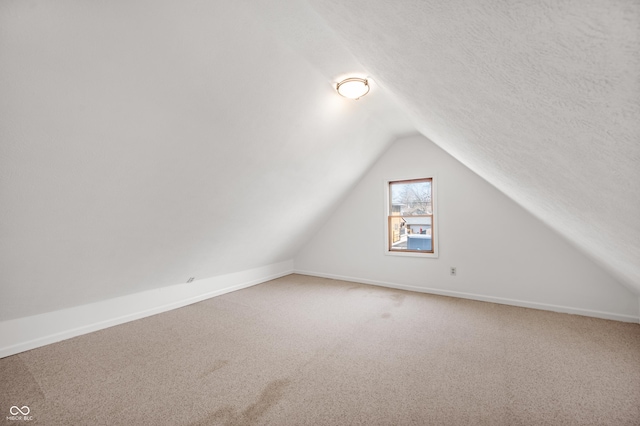 bonus room featuring vaulted ceiling, light colored carpet, baseboards, and a textured ceiling