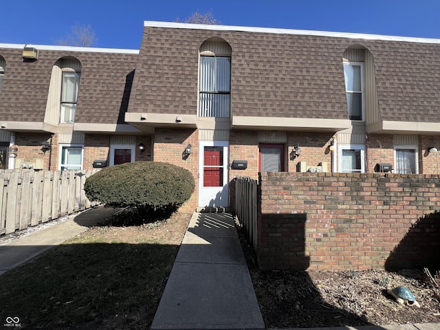 view of property featuring brick siding, mansard roof, and roof with shingles