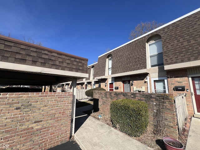 view of side of home featuring a fenced front yard, mansard roof, brick siding, and roof with shingles