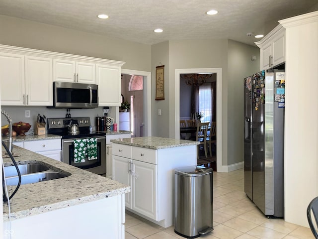 kitchen with light stone counters, recessed lighting, stainless steel appliances, white cabinetry, and a center island