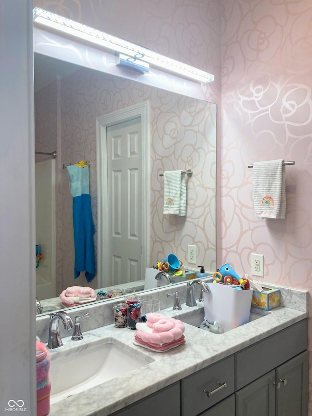 full bath with wallpapered walls, double vanity, and a sink