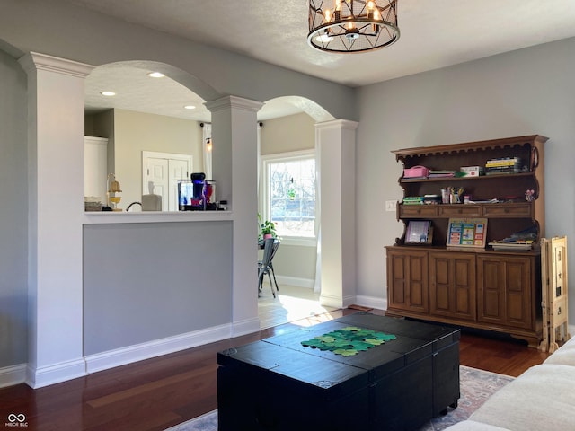 living room featuring wood finished floors, baseboards, ornate columns, recessed lighting, and arched walkways