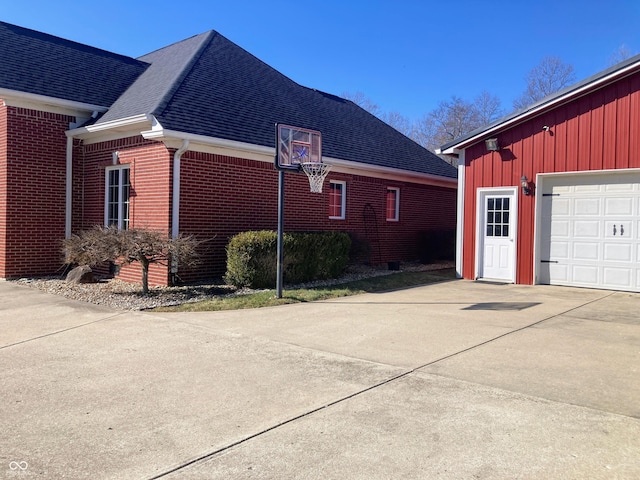 view of property exterior with a garage, brick siding, roof with shingles, and driveway