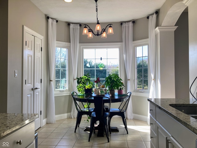 dining area featuring light tile patterned floors, baseboards, a healthy amount of sunlight, and a chandelier