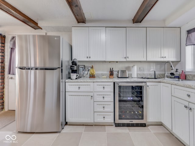 kitchen featuring wine cooler, beam ceiling, freestanding refrigerator, light tile patterned flooring, and white cabinetry