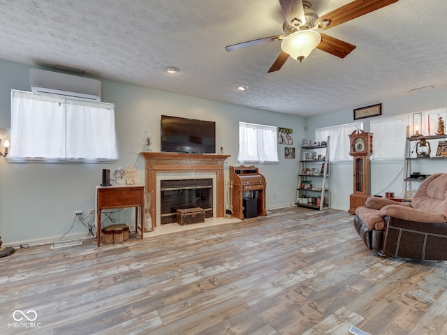 living room featuring a wall unit AC, a fireplace with flush hearth, wood finished floors, and a textured ceiling