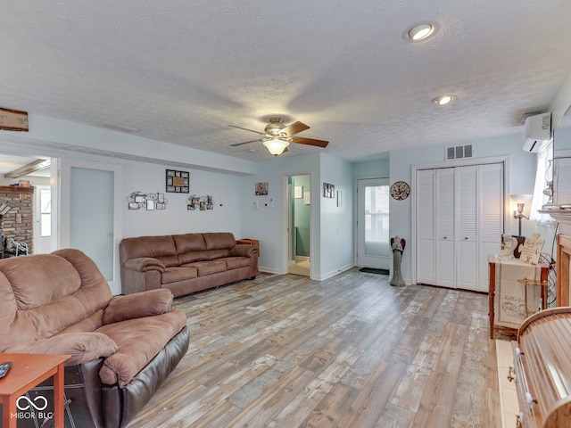 living area featuring visible vents, a stone fireplace, an AC wall unit, and light wood finished floors