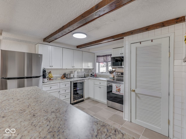 kitchen with beverage cooler, light tile patterned flooring, stainless steel appliances, white cabinetry, and beamed ceiling