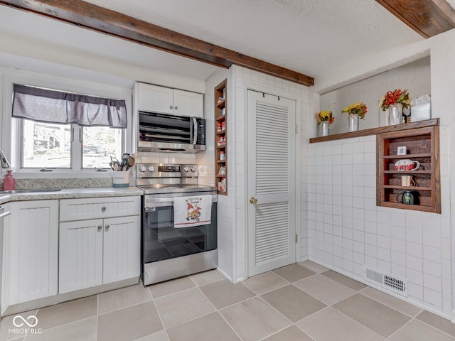 kitchen with visible vents, beam ceiling, stainless steel appliances, white cabinetry, and a sink