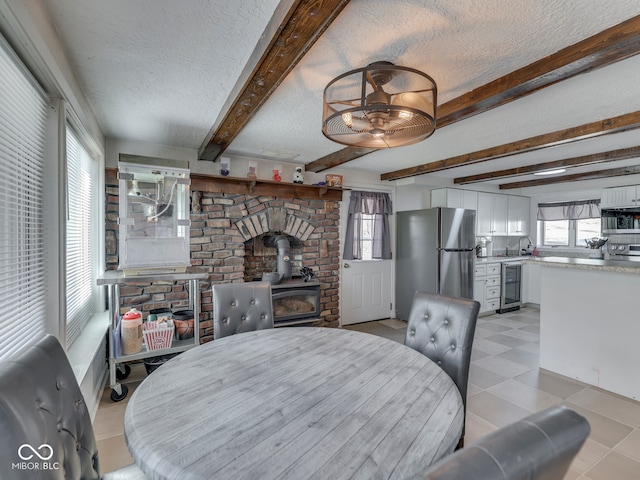 dining space with beverage cooler, beam ceiling, a textured ceiling, and a wood stove