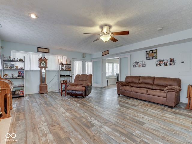 living room with ceiling fan, a textured ceiling, and light wood-style flooring