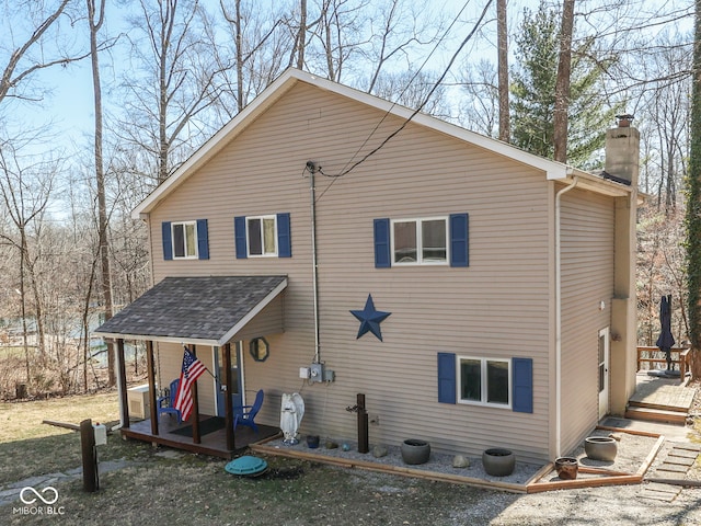 rear view of house featuring a chimney and a shingled roof