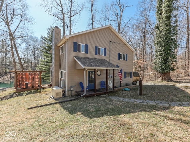 rear view of property featuring a deck, a chimney, a yard, and roof with shingles