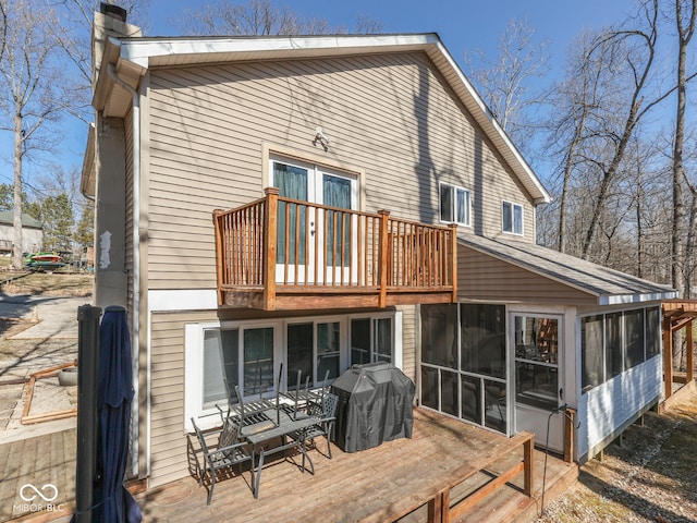 back of property with a deck, a chimney, and a sunroom