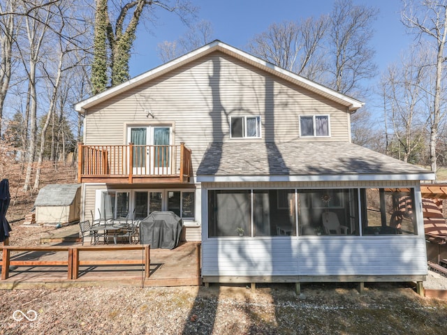 back of property with an outbuilding, a storage shed, a shingled roof, and a sunroom