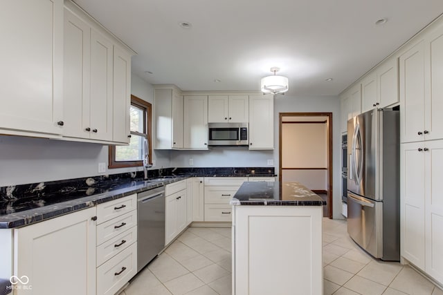 kitchen with a sink, a center island, appliances with stainless steel finishes, light tile patterned flooring, and white cabinets