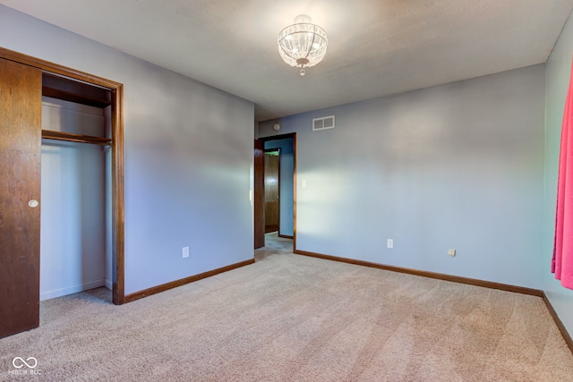 unfurnished bedroom with baseboards, visible vents, a closet, carpet flooring, and a notable chandelier