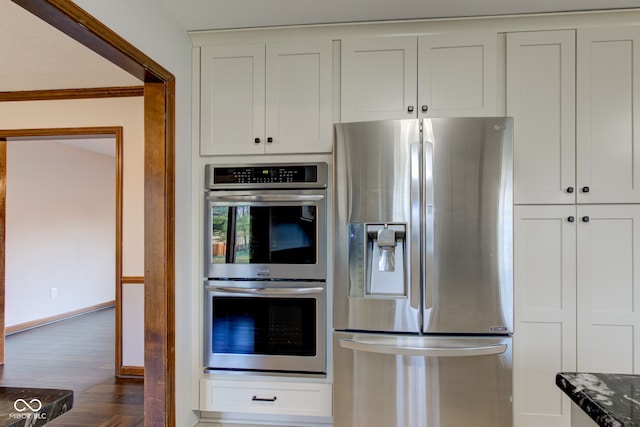 kitchen with dark wood-type flooring, baseboards, dark stone countertops, white cabinets, and stainless steel appliances