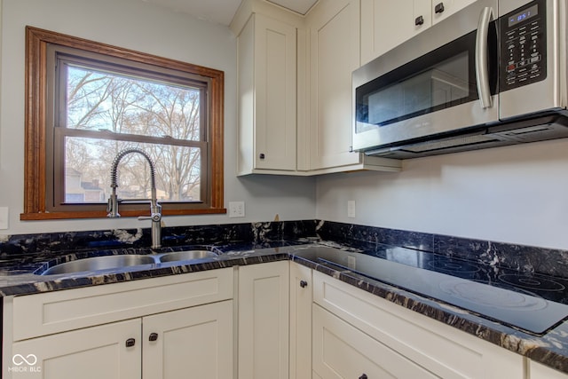 kitchen with a sink, stainless steel microwave, dark stone counters, white cabinets, and black electric cooktop