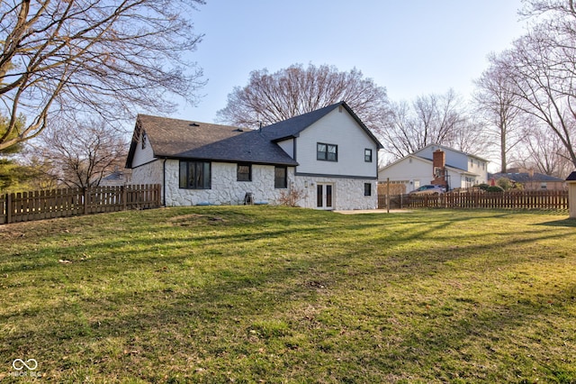 back of property with roof with shingles, a fenced backyard, french doors, stone siding, and a lawn