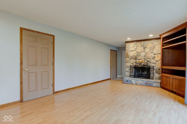 unfurnished living room with a stone fireplace, baseboards, and light wood finished floors